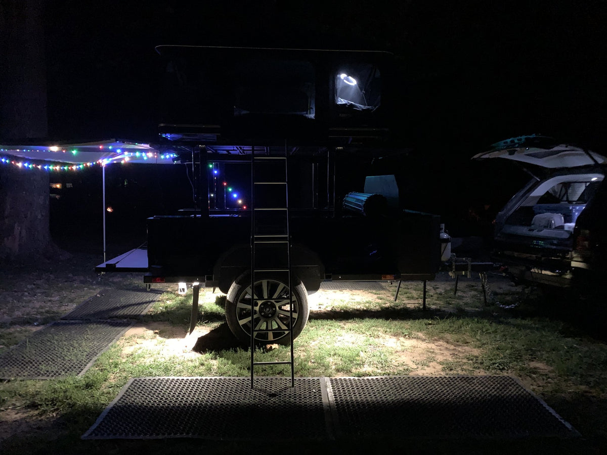 Evening view of the camp setup with the trailer's ladder down and ground lighting on — photo 14