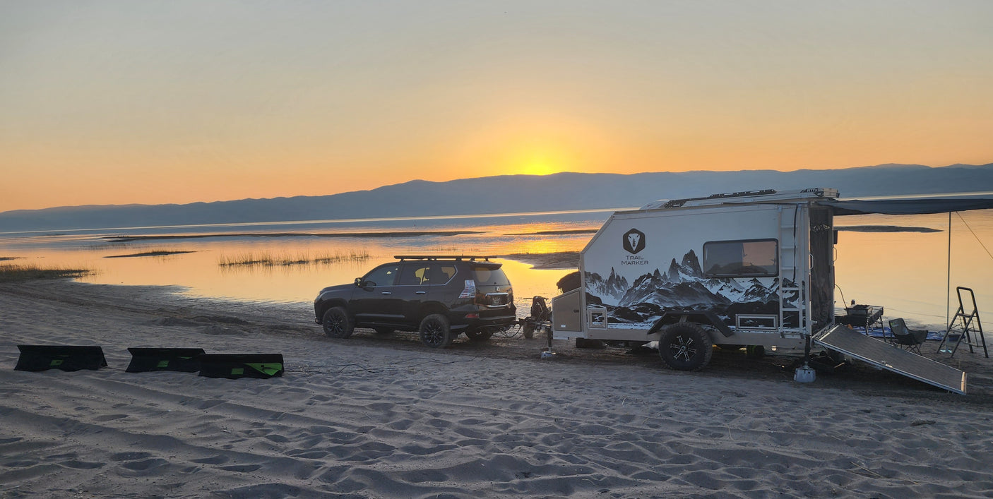 Trail Marker overland trailer with awning extended at a lakeside sunset
