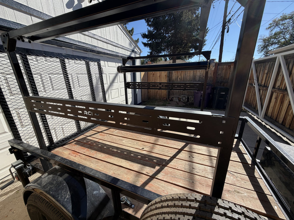 Deck-level view of the slotted RCI accessory crossbar mounted across the rack with the black roller bar above it, showing the deck tie-down track and the mesh gate standing at the rear — photo 8