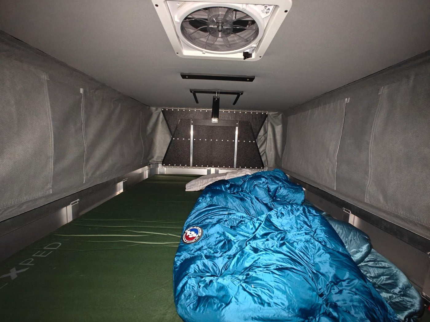 Camper interior looking forward, Maxxair Deluxe fan overhead and the sleeping platform below — photo 13