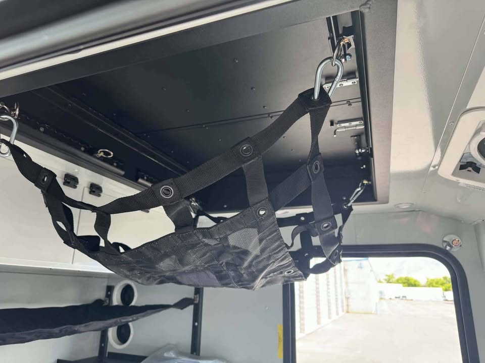 Close-up of the gear and bunk hammock system inside the XPedition Voyager Sky XE, clipped to overhead anchor points beneath the raised hatch panel — photo 9