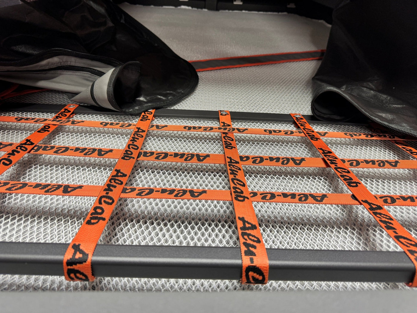Close view of the rooftop tent's sleeping platform with the white breathable mesh mattress base and the orange Alu-Cab branded webbing straps laid across it — photo 6
