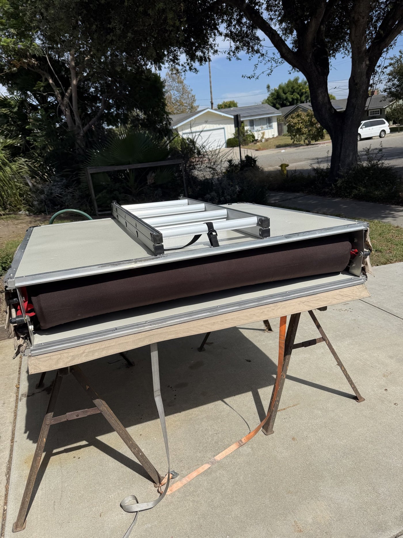 The tent folded closed on sawhorses showing the aluminum base pan, mattress edge and the sectioned telescoping ladder stowed on top — photo 11
