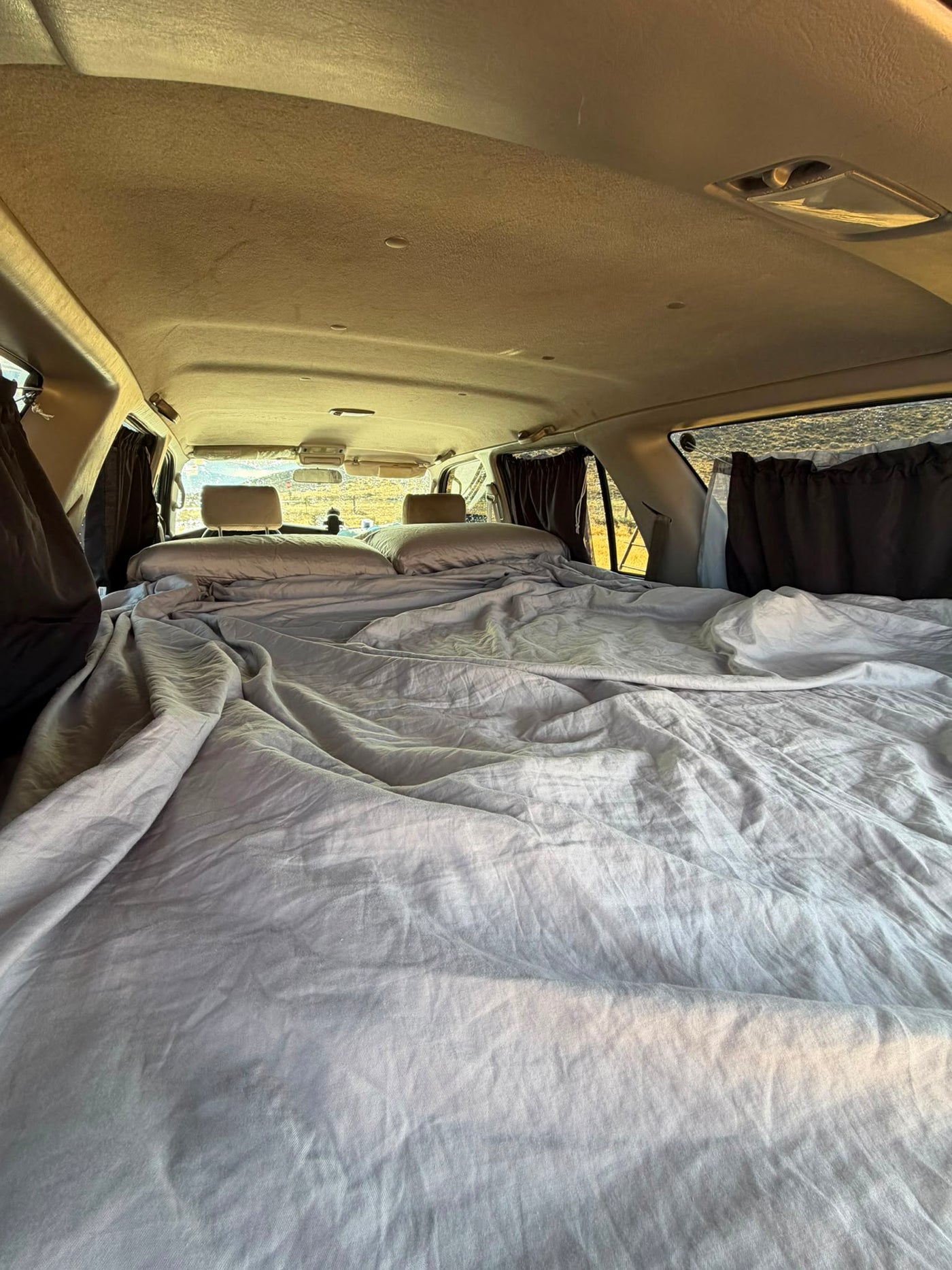 Full-length view of the sleeping platform from the cargo area toward the front seats, showing the flat two-person bed and side curtains — photo 7