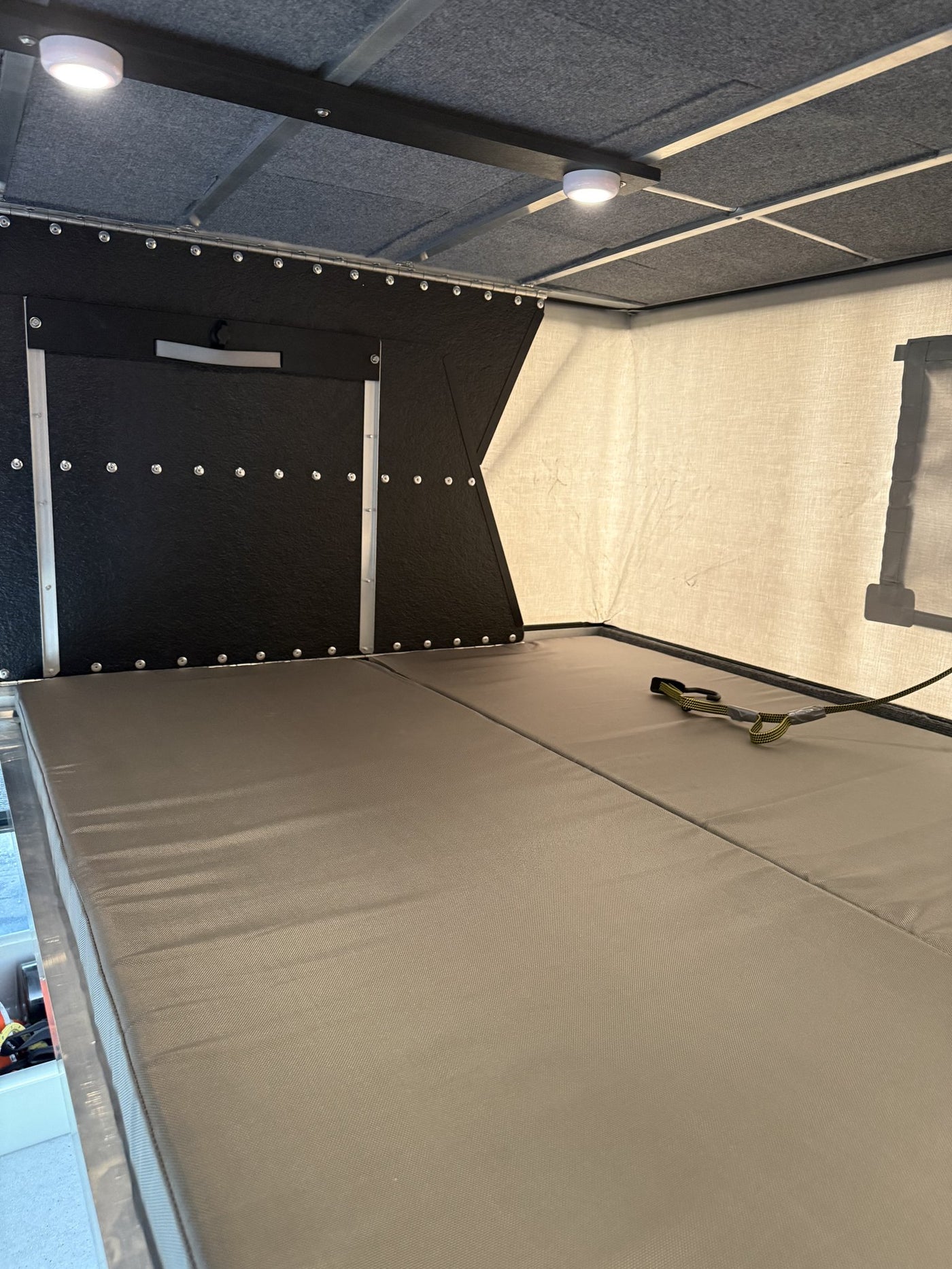 Interior view of the sleeping area with the north-south foam mattress platforms laid out edge to edge, the insulated canvas side wall with a window cover, LED puck lights overhead and the black insulated front wall — photo 4