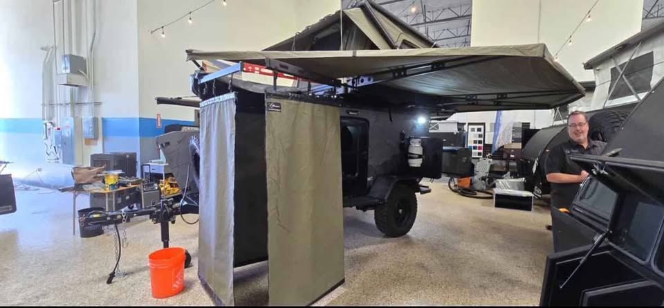 Bush Company Outpost shower enclosure set up alongside the XPedition Voyager Sky XE indoors, hanging from the awning rail with the awning extended overhead — photo 17