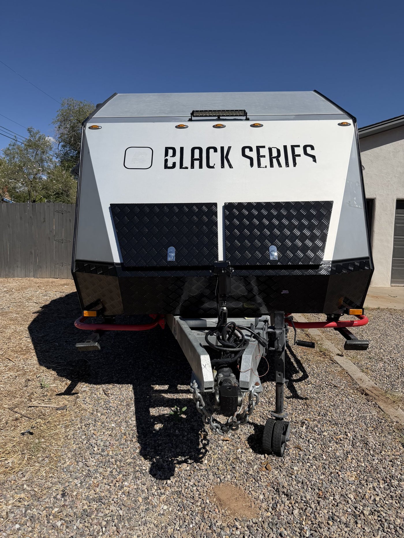 Head-on front view of the trailer showing the angled aerodynamic nose, roof-mounted LED light bar, checker-plate stone guards, articulating hitch coupler with safety chains and the upgraded power tongue jack — photo 4