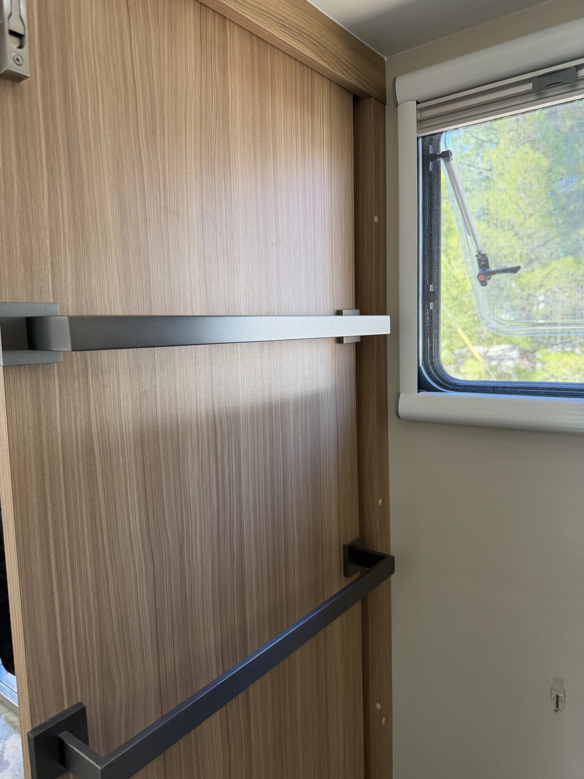 Interior wood-grain door with towel rails, alongside a side window with roller blind and flyscreen — photo 16