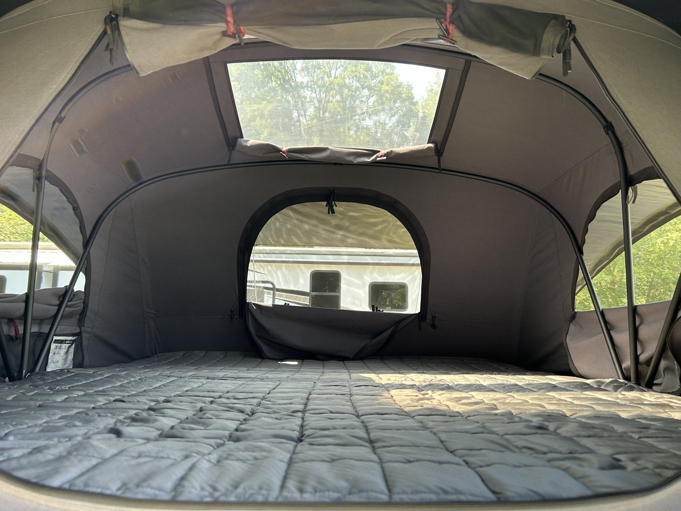 Interior of the rooftop tent looking out through the arched doorway and upper window, showing the quilted mattress, the interior insulation liner and the black support poles — photo 4