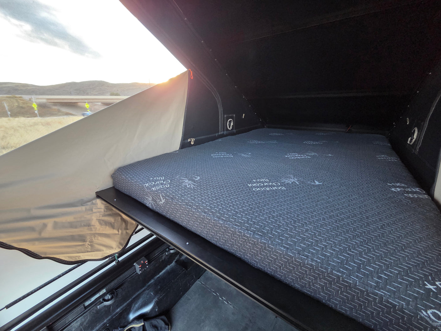 RV rental rooftop tent interior: comfy Bamboo Charcoal mattress, ready for camping trips. Outdoor views visible.