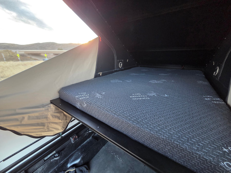 RV rental rooftop tent interior: comfy Bamboo Charcoal mattress, ready for camping trips. Outdoor views visible.