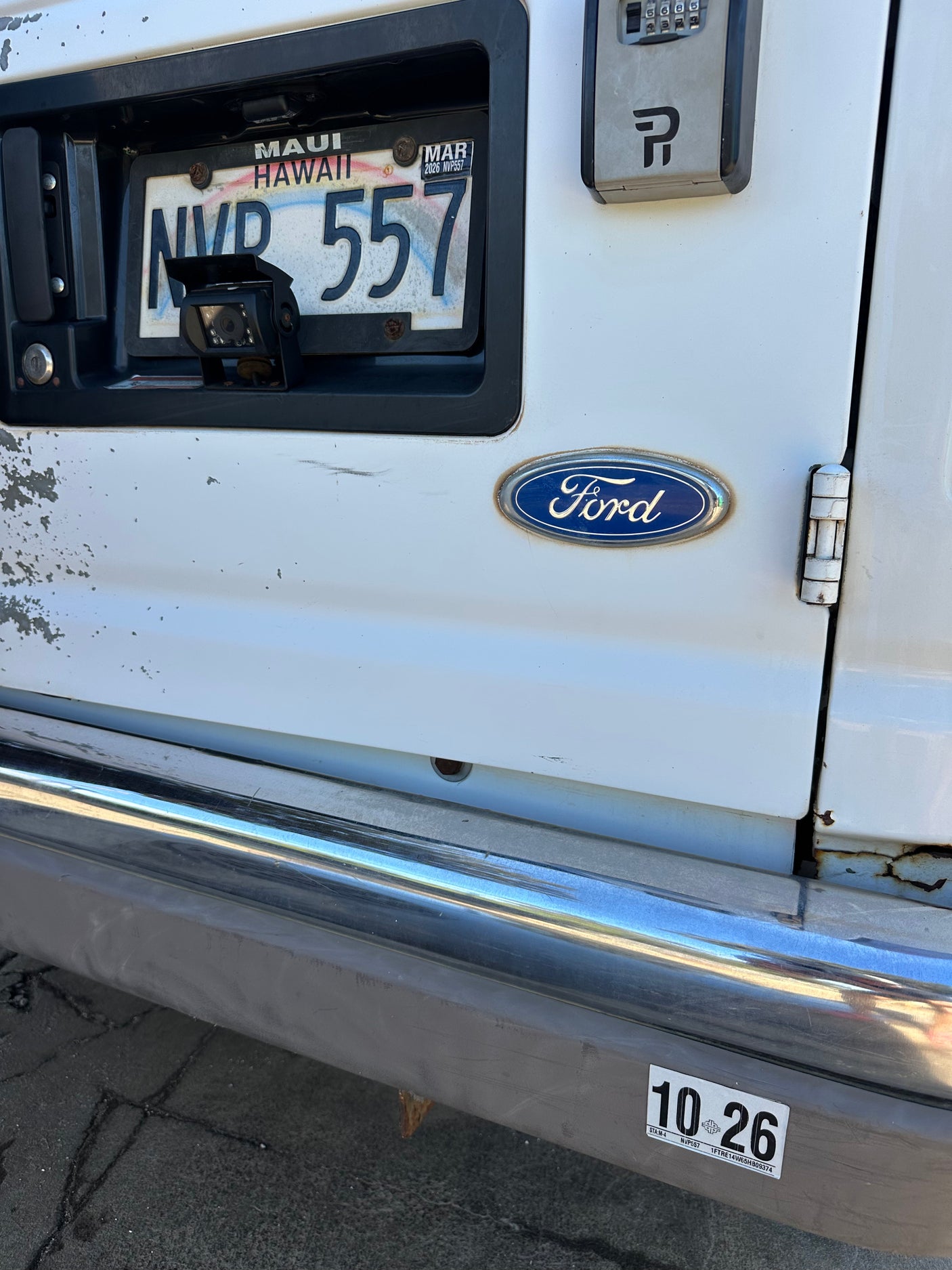 Hawaii rv rental Ford van's rear. Shows NVR 557 license (exp. Mar 2026), backup camera, and key lockbox.