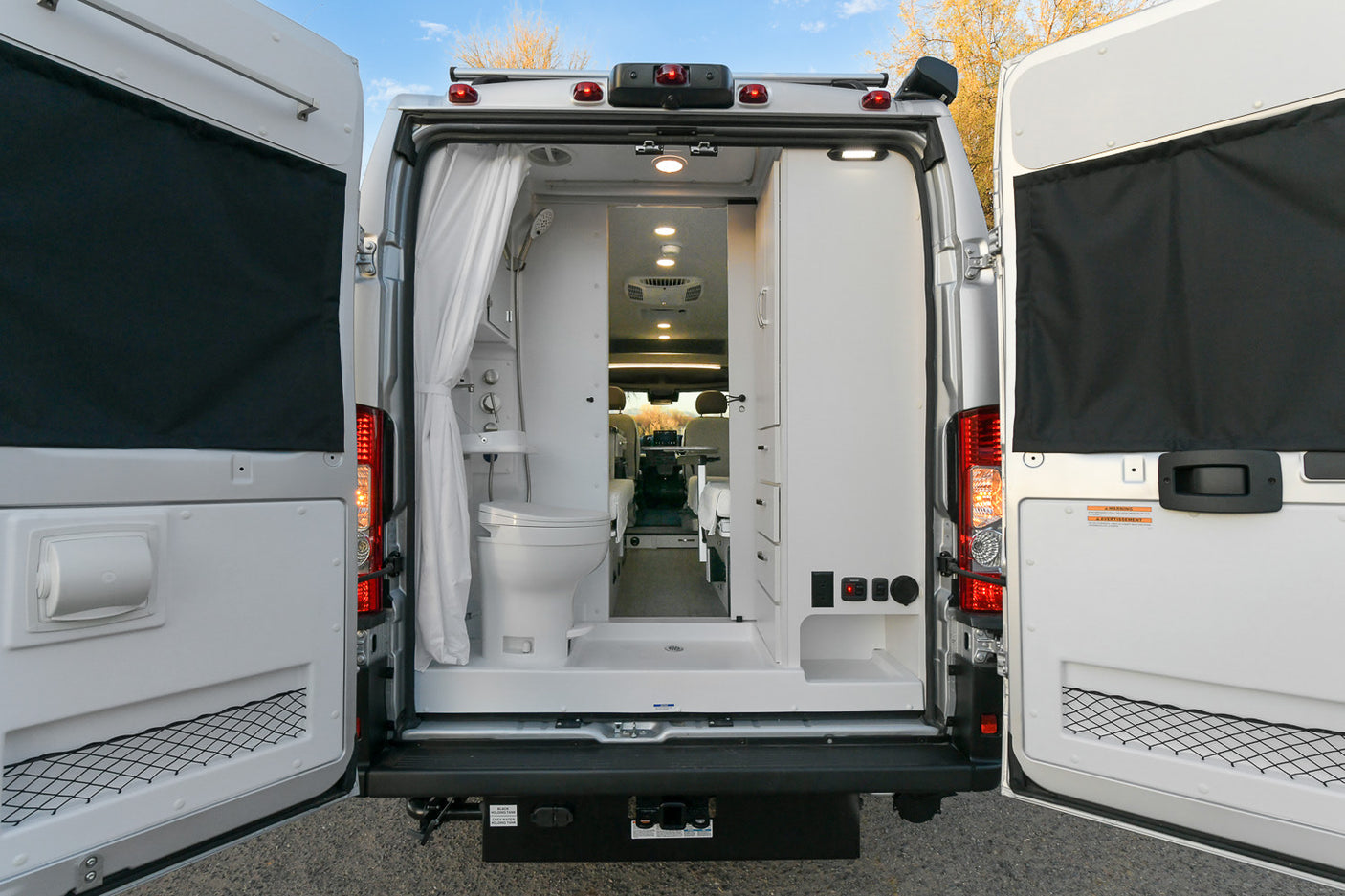 RV rental with open rear doors, revealing its interior: a compact bathroom with shower and toilet on the left, and storage on the right.