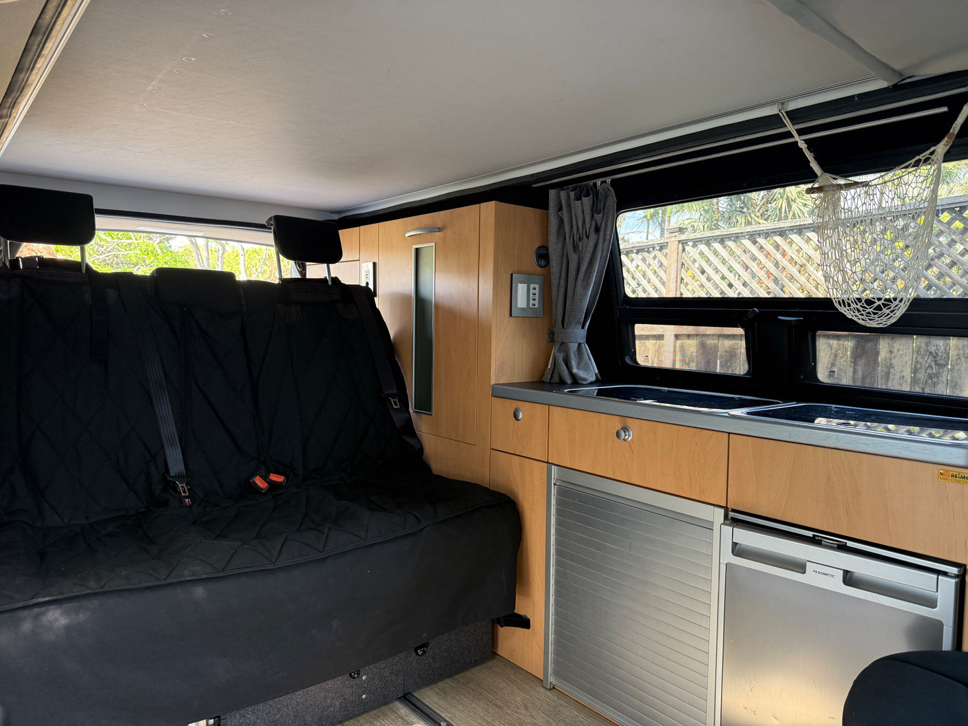 Bright rv rental interior: versatile black bench seat/bed, compact kitchenette with sinks, Dometic fridge & wood cabinets.
