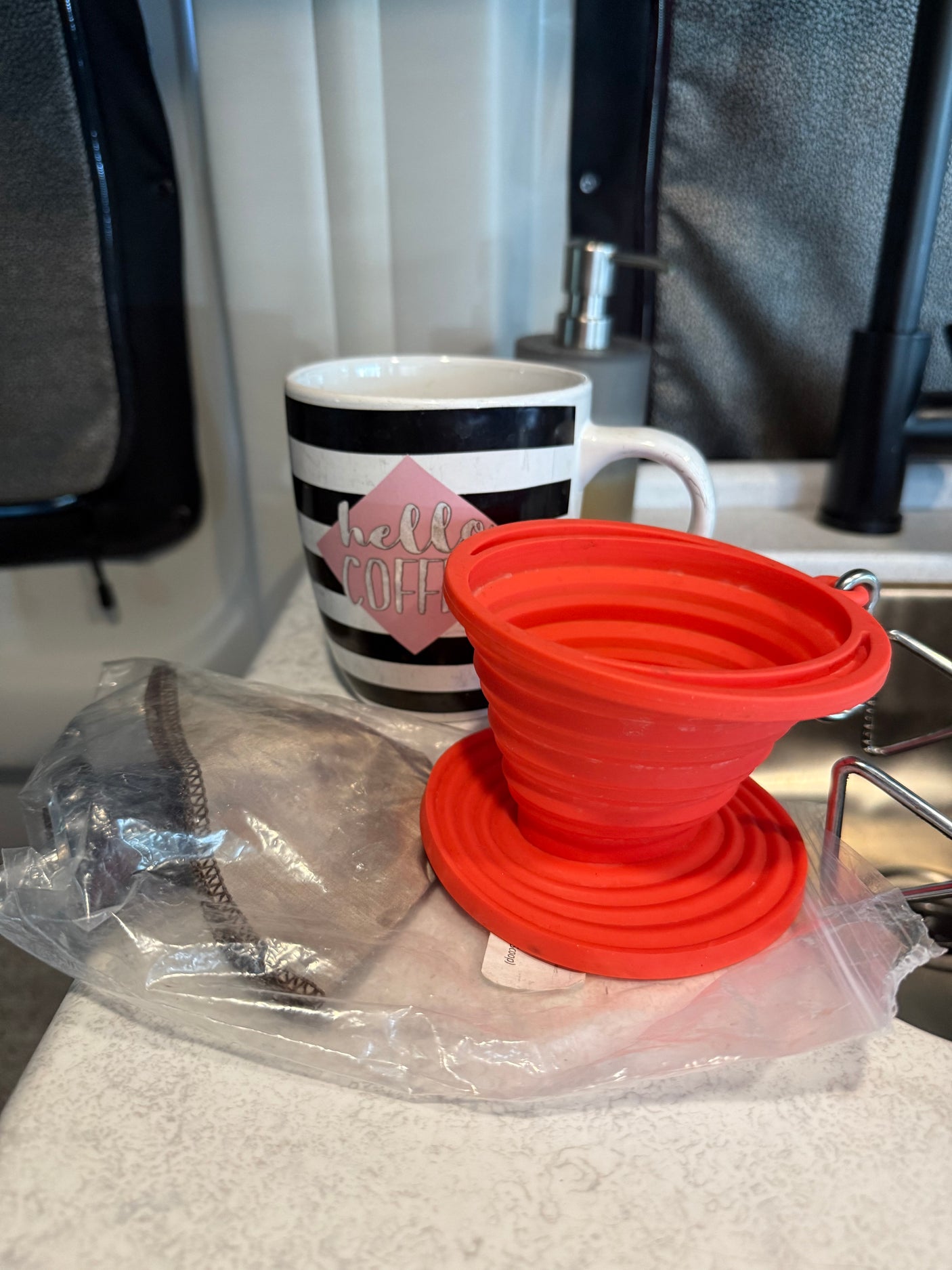RV rental coffee setup: a "hello COFFEE" mug, portable pour-over filter, and mesh filter for your morning brew.
