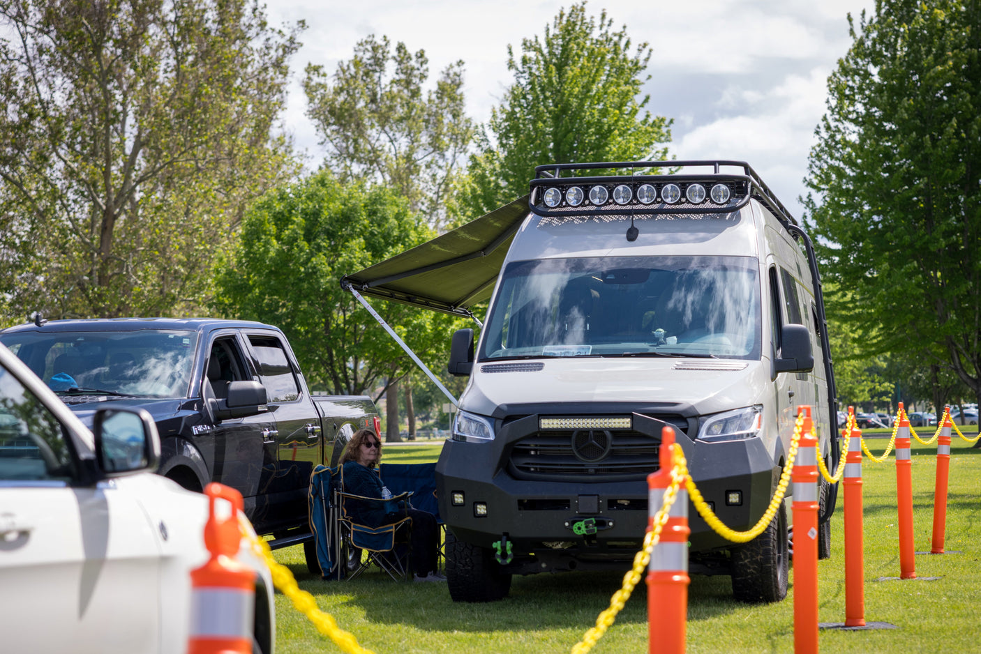 A robust, modified Sprinter camper van, perfect for an rv rental adventure, featuring an extended awning and roof-mounted lights.