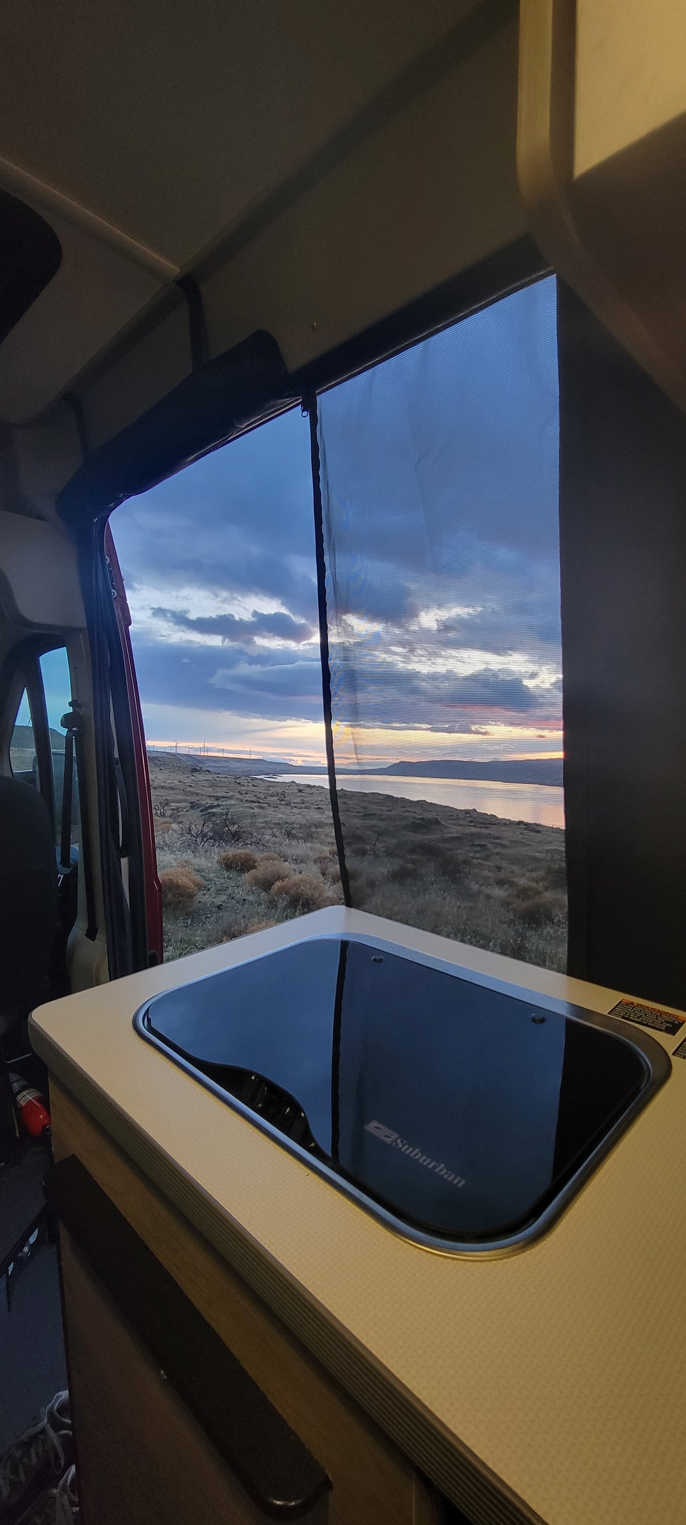 RV rental sunset view: A peaceful evening scene from inside a camper van, featuring a large screen window and kitchen sink.