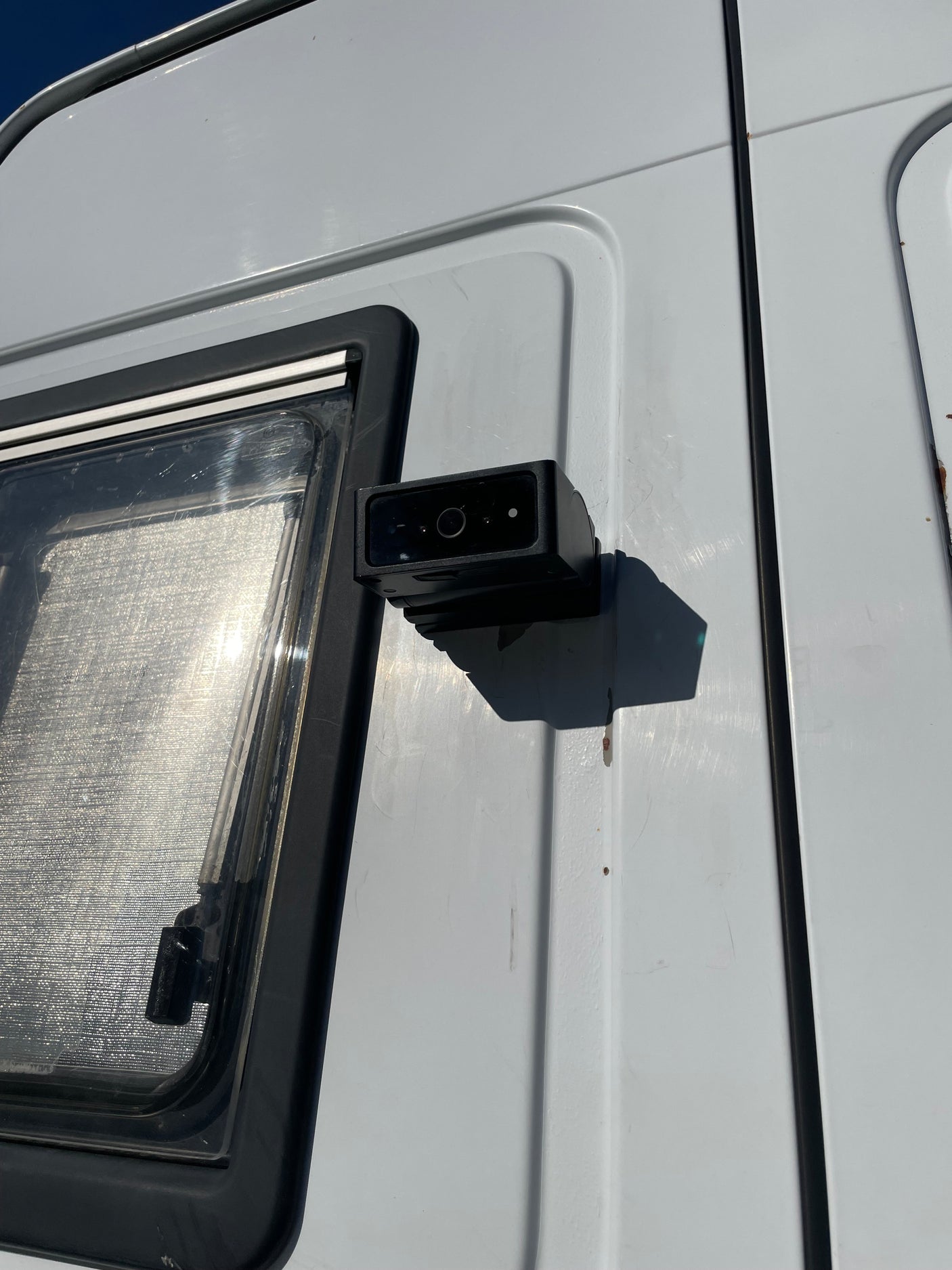 Detail of an **rv rental** side: a mounted black camera/sensor next to a window with a textured interior, showing minor wear.