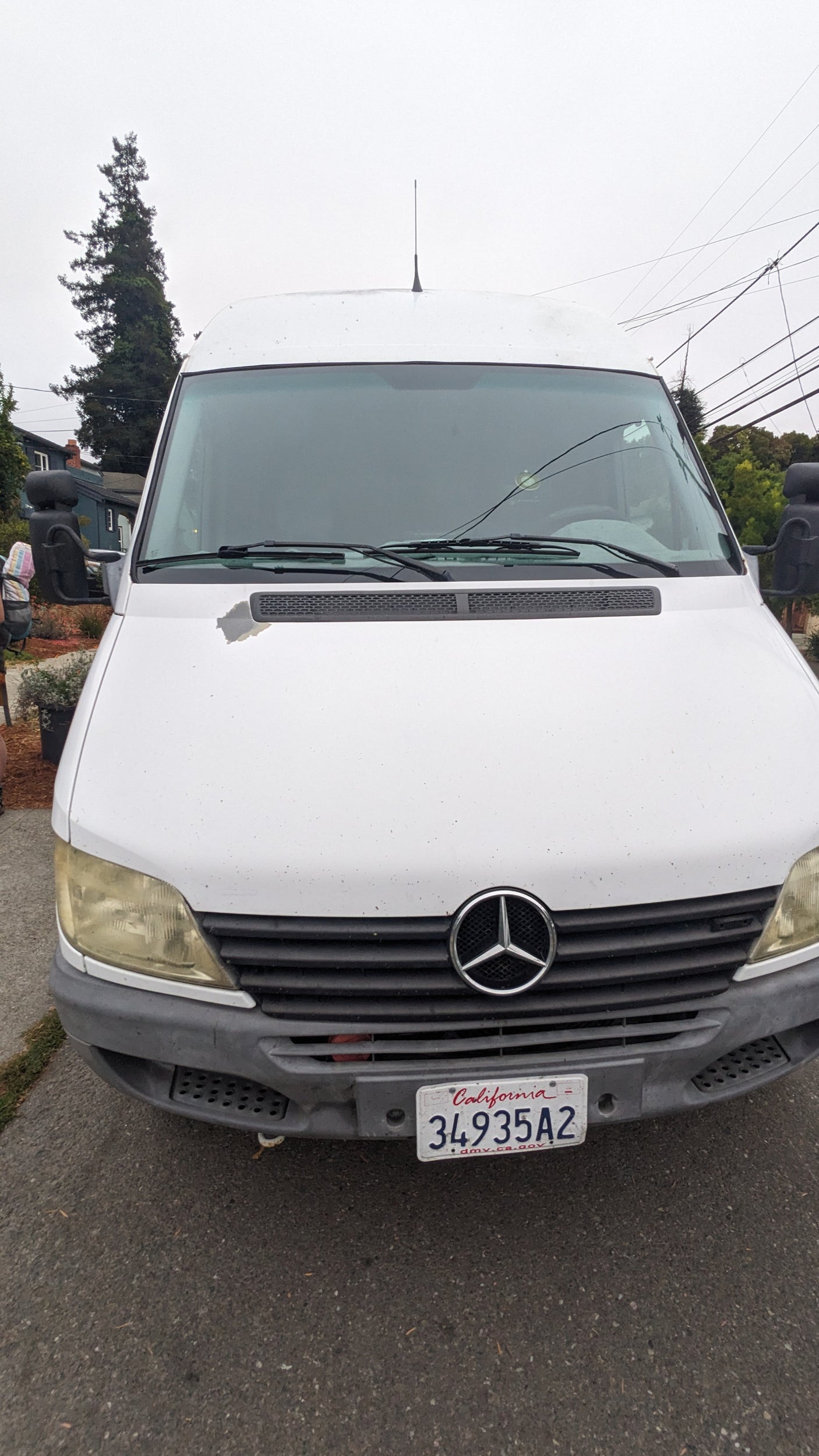 White Mercedes-Benz Sprinter van, a common RV rental choice. Features CA plate, peeling paint, and yellowed headlights.