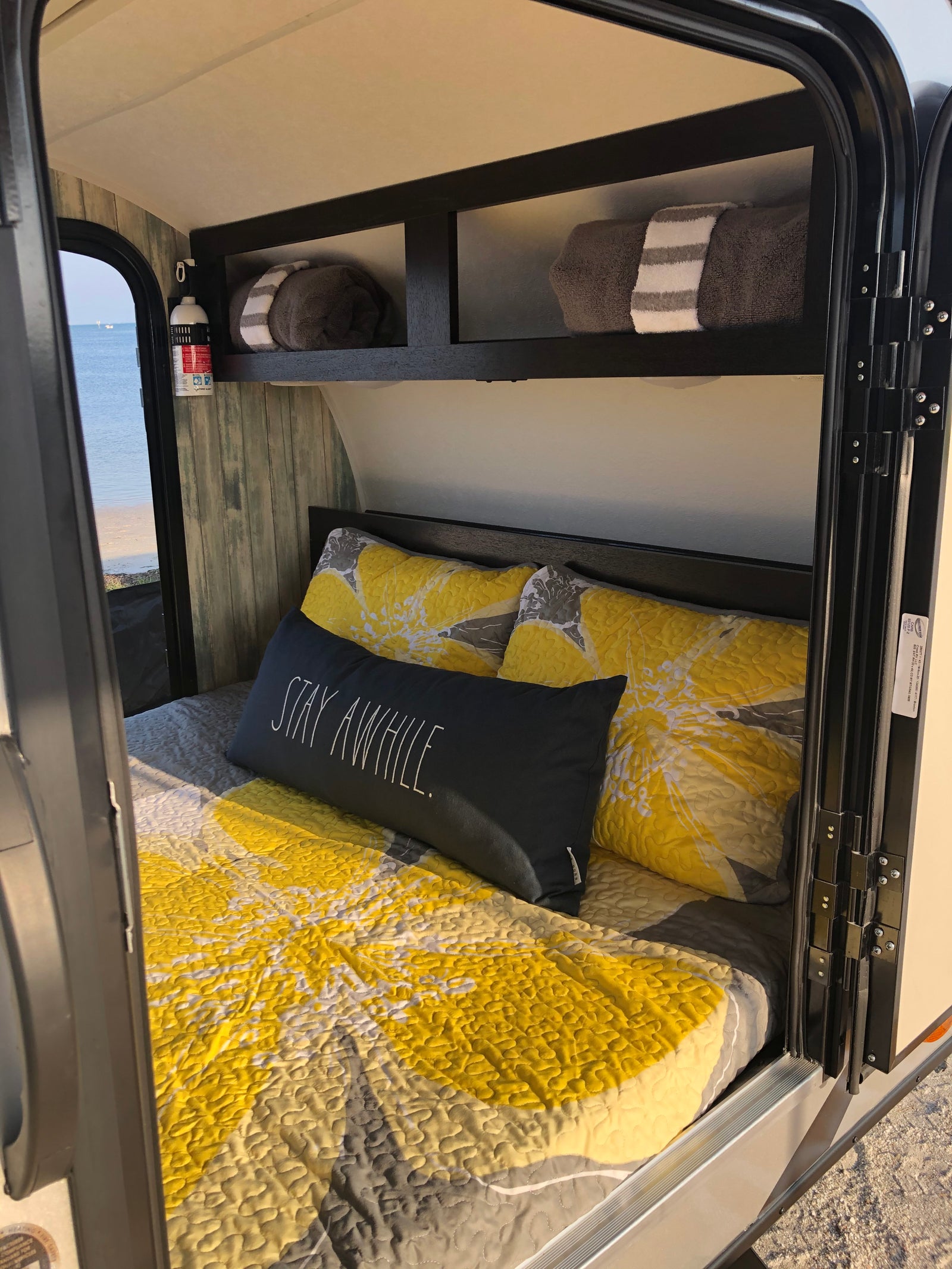 Cozy RV rental interior with yellow bedding and ocean view, featuring a comfortable bed for a relaxing stay.