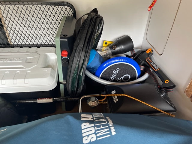 Inside an RV rental, camping gear including a cooler, portable stove, Bose speaker, and hatchet are stored.