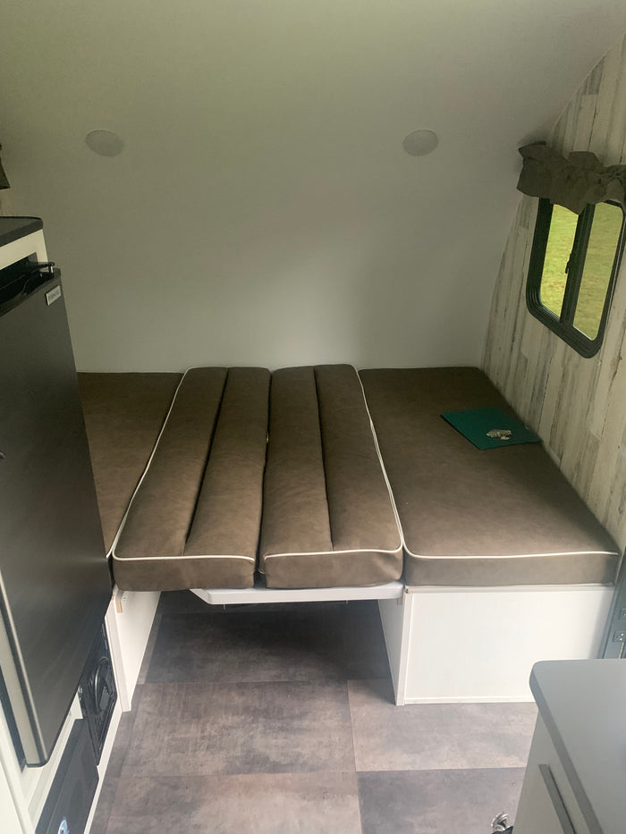 RV rental: Compact camper interior with brown upholstered bed/seating, compact refrigerator, and window view.