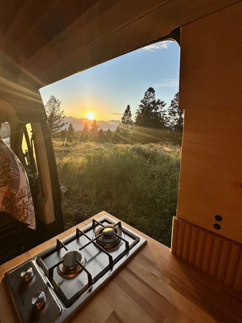 Experience epic sunrises from your RV rental! This camper van's kitchen stove offers mountain & forest views.