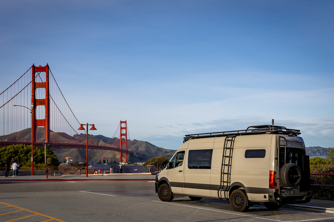 Tan RV rental van parked near the Golden Gate Bridge, San Francisco. Features a roof rack and ladder.