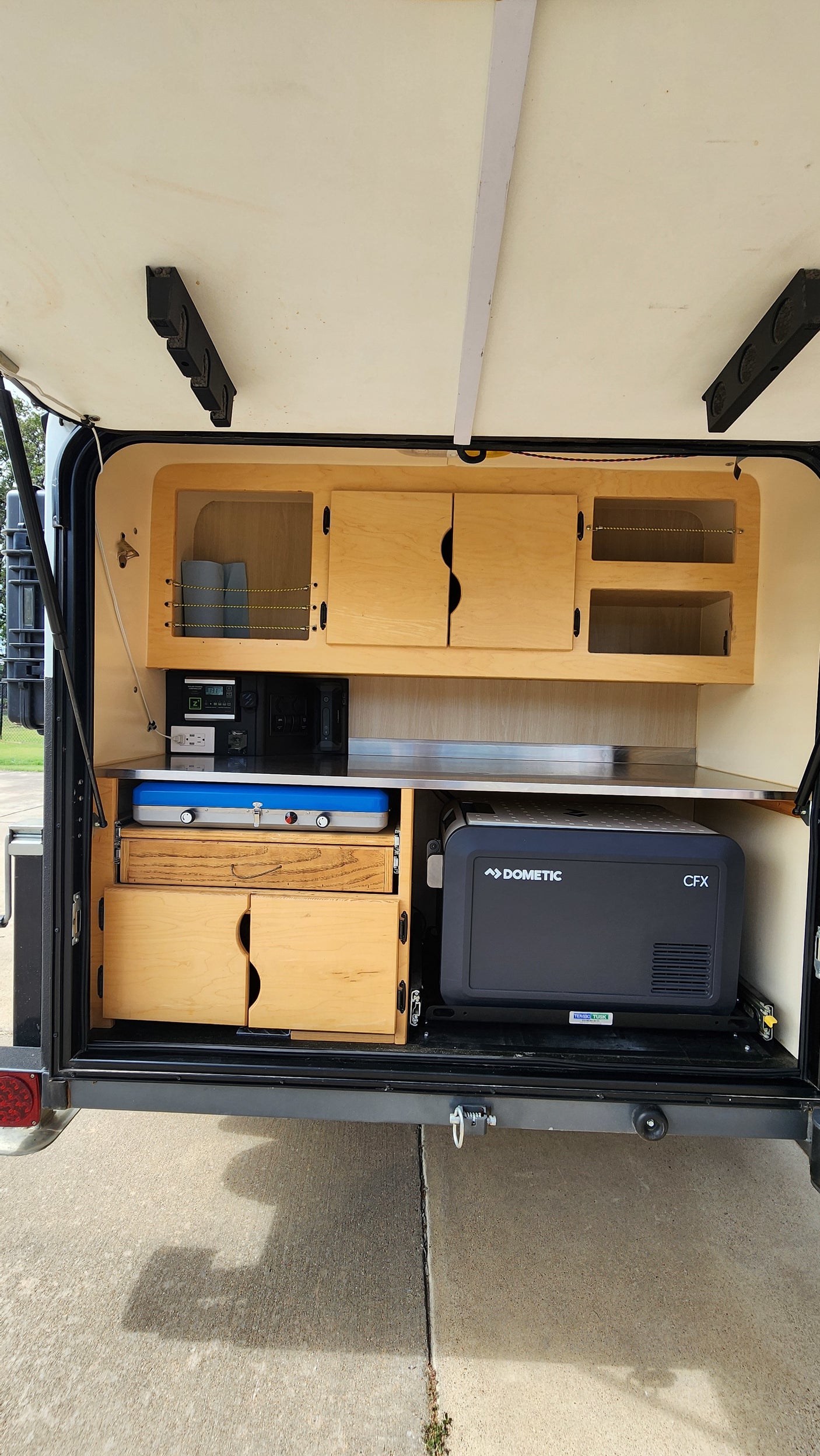 RV rental teardrop trailer's rear galley features a Dometic fridge, portable stove, Zamp power system, and wood cabinets. Ideal for camping.