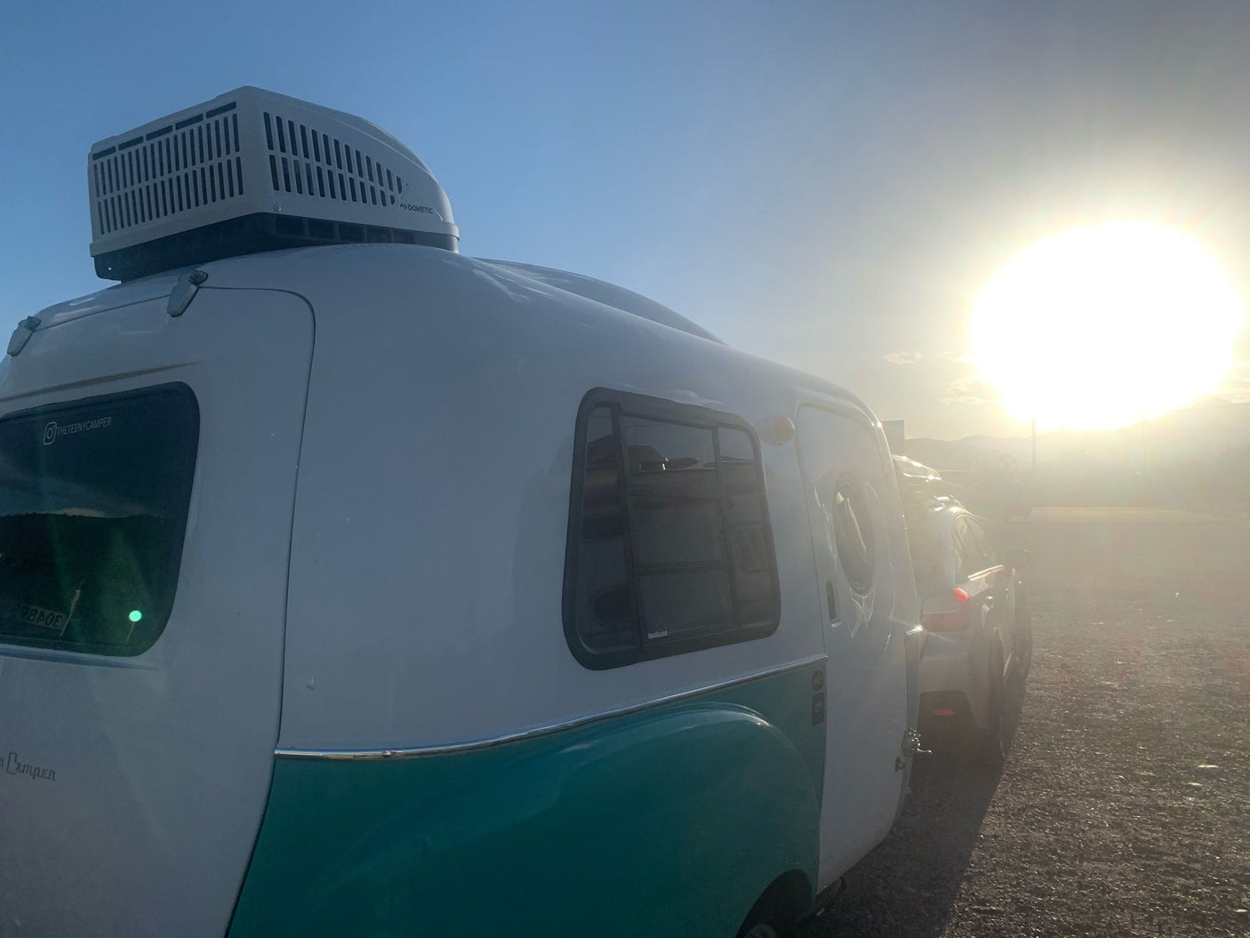 Side view of a white & teal retro camper with a Dometic AC unit, ideal for an RV rental. Bright sun.