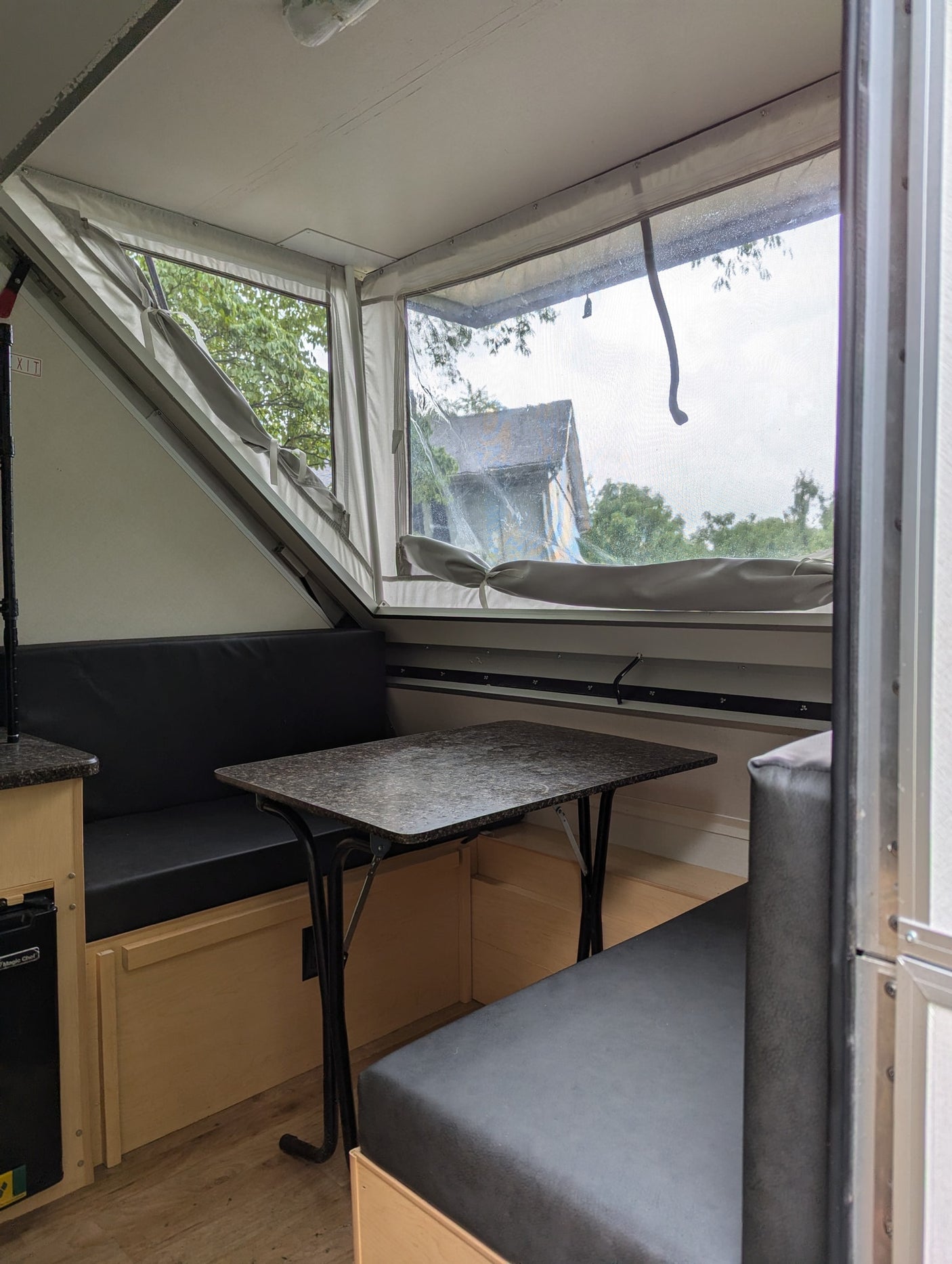 Inside an RV rental: a compact, light-filled dinette with black bench seating and a patterned table, looking out to trees.