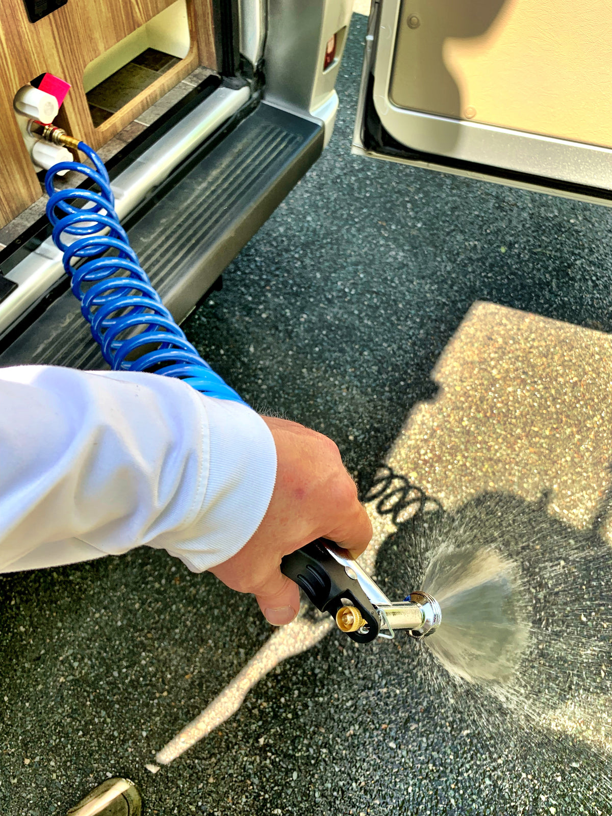 Hand spraying water from a coiled hose connected to an RV rental's outdoor shower port, perfect for cleaning. — photo 16