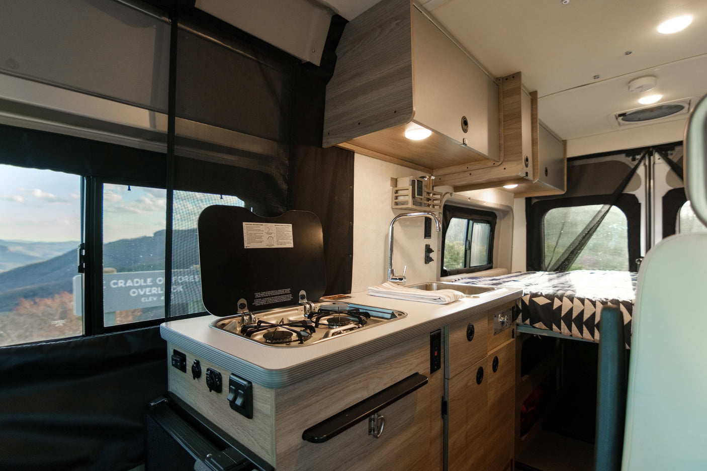 stands at a scenic mountain overlook under a beautiful blue sky.|Cozy rv rental bedroom features a geometric blue/white quilt