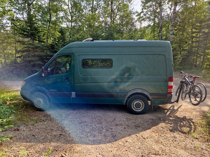 and comfy seating/bed.|Green Mercedes Sprinter RV rental van with bikes parked on a forest dirt road