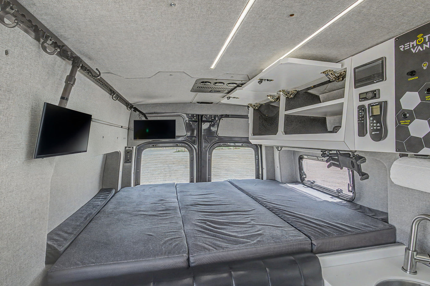This spacious rv rental camper van interior features a comfy bed, dual TVs, kitchen area, and control panel for ultimate comfort.