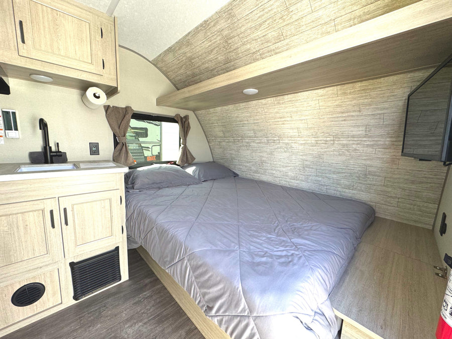 Cozy interior of an RV rental featuring a comfortable bed, kitchenette with sink, and overhead storage. Ideal for travel.