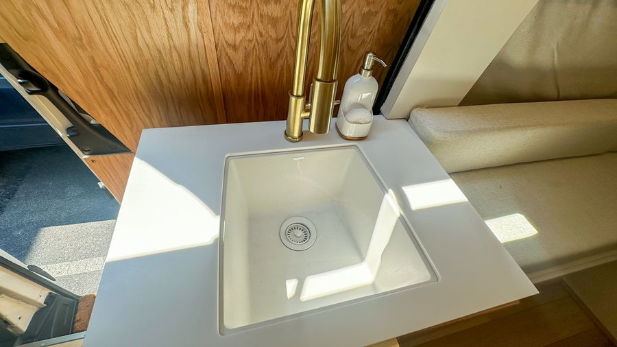 white counter with cooktop.|Step into this chic RV rental! Features a compact kitchen with a sink