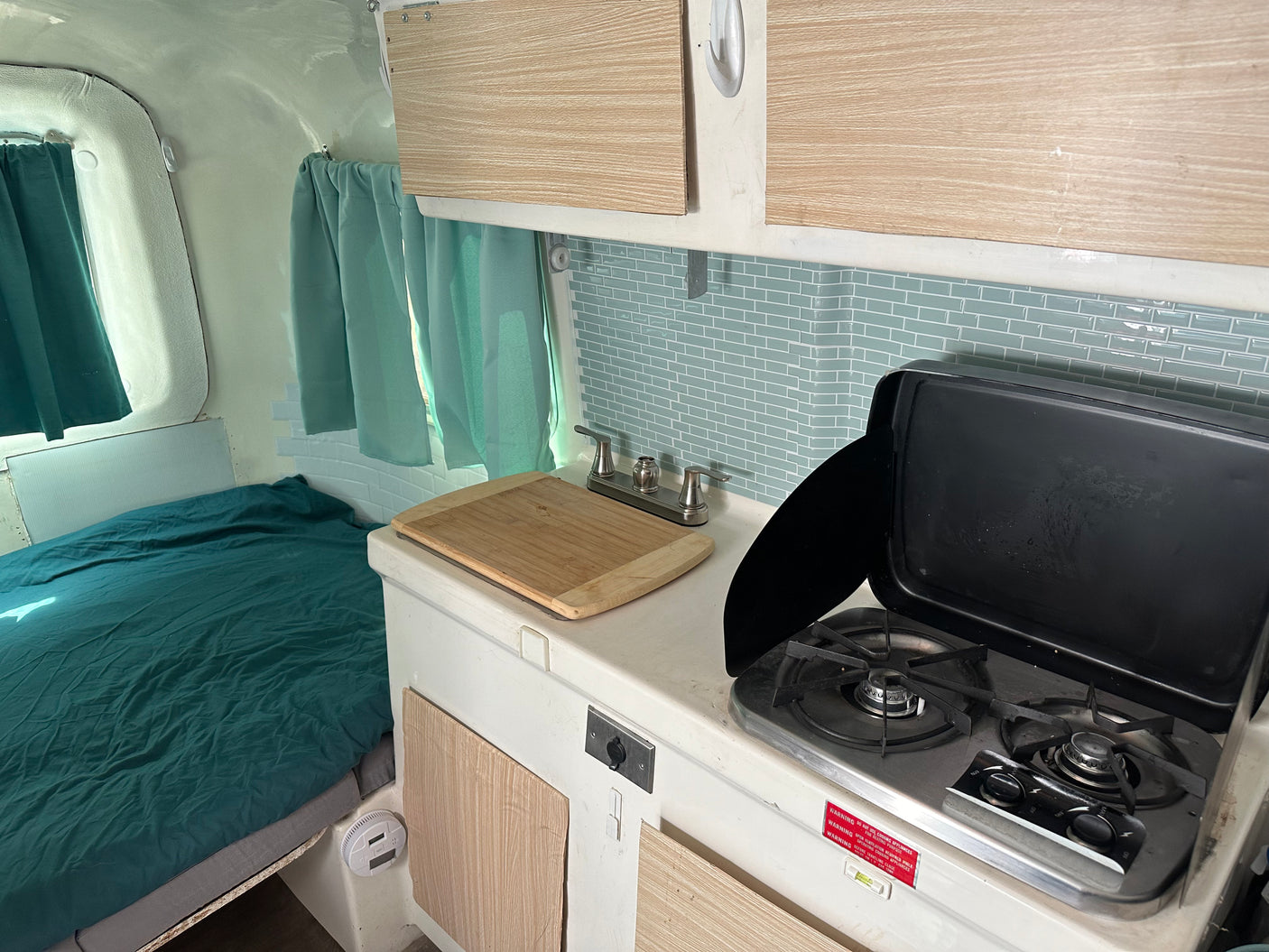Cozy RV rental interior with a compact kitchen featuring a stove, sink, and backsplash, plus a comfortable bed.