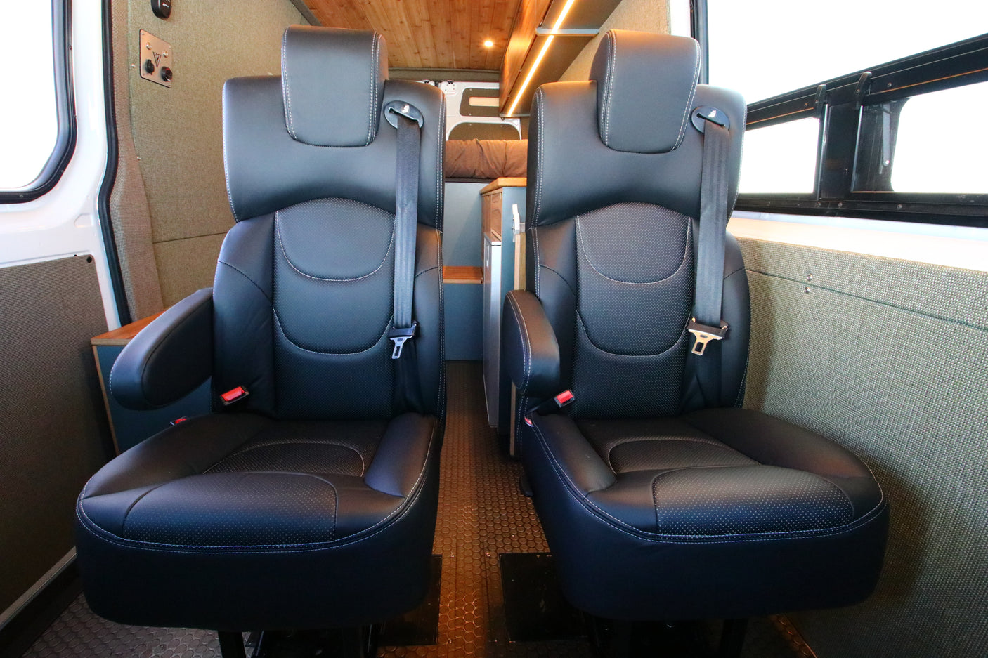 Two black leather captain's chairs with seatbelts offer comfortable passenger seating in this RV rental van interior.