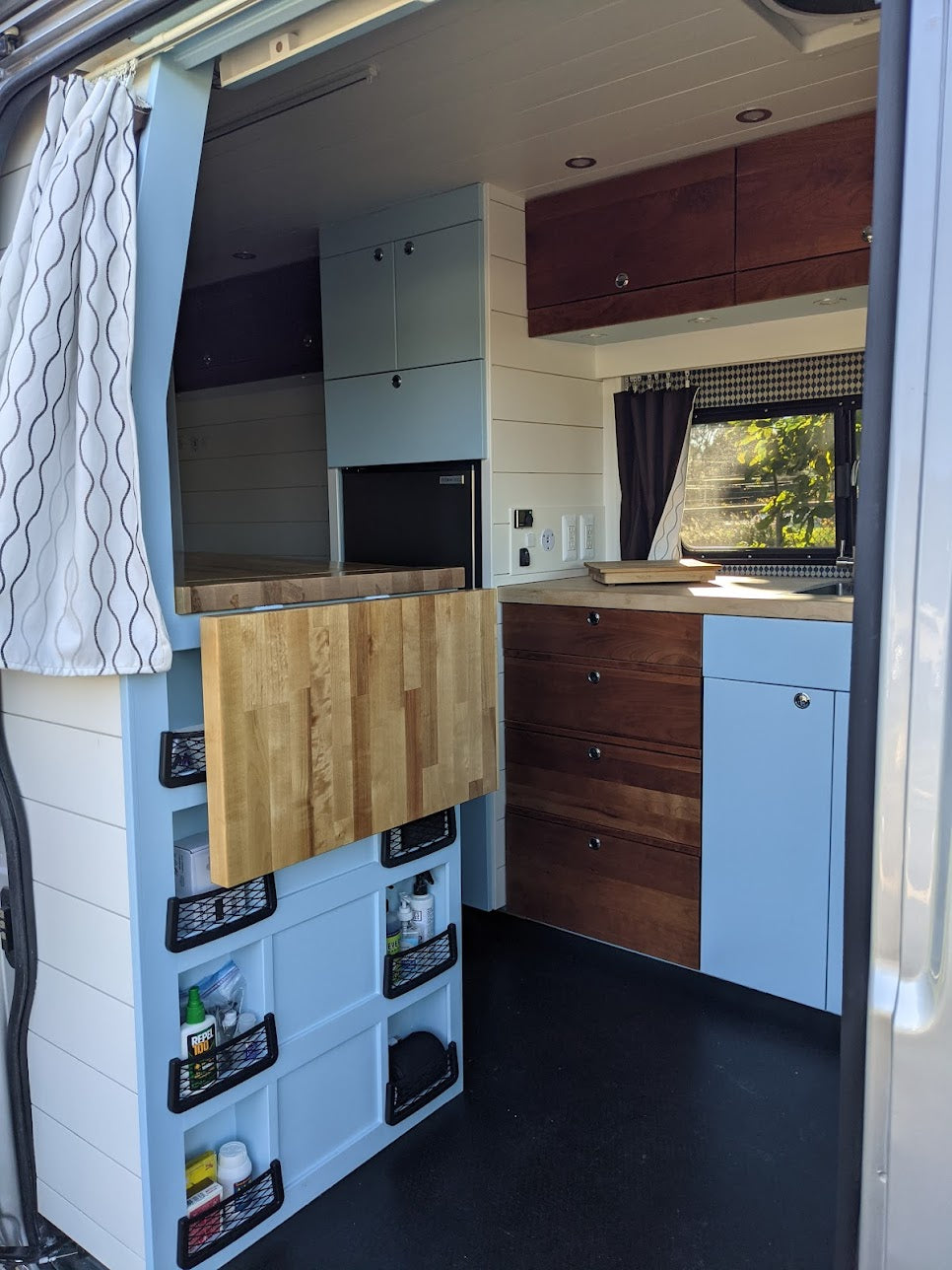 This RV rental features a compact kitchen with light blue cabinets, wood countertops, and clever storage for mobile living.