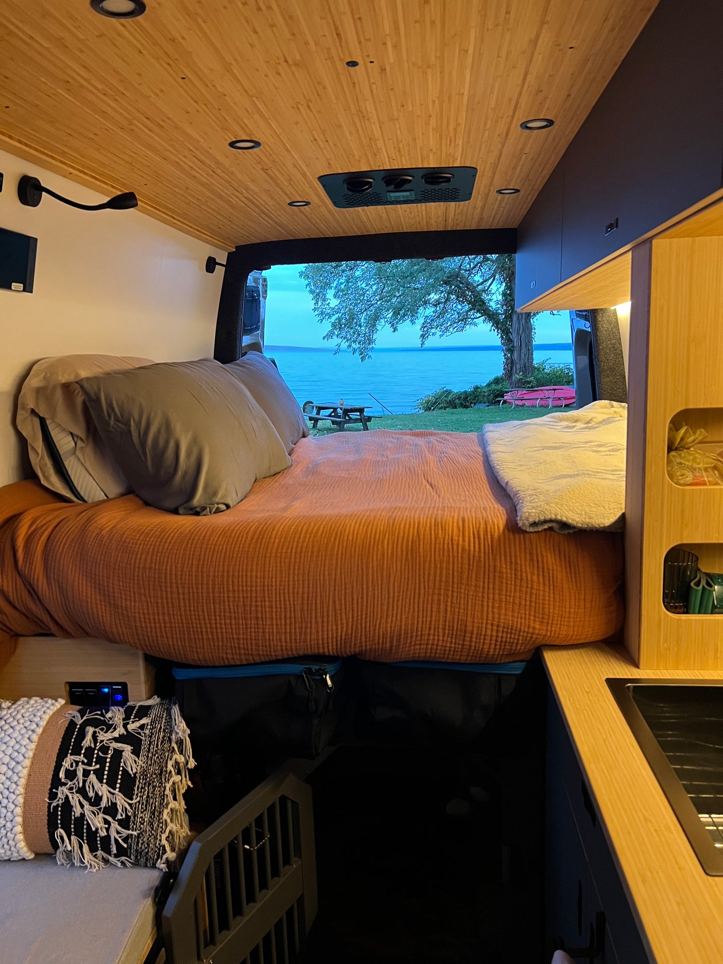 Cozy rv rental interior featuring a comfy bed, modern wooden ceiling, and a stunning lake view from the open rear doors.