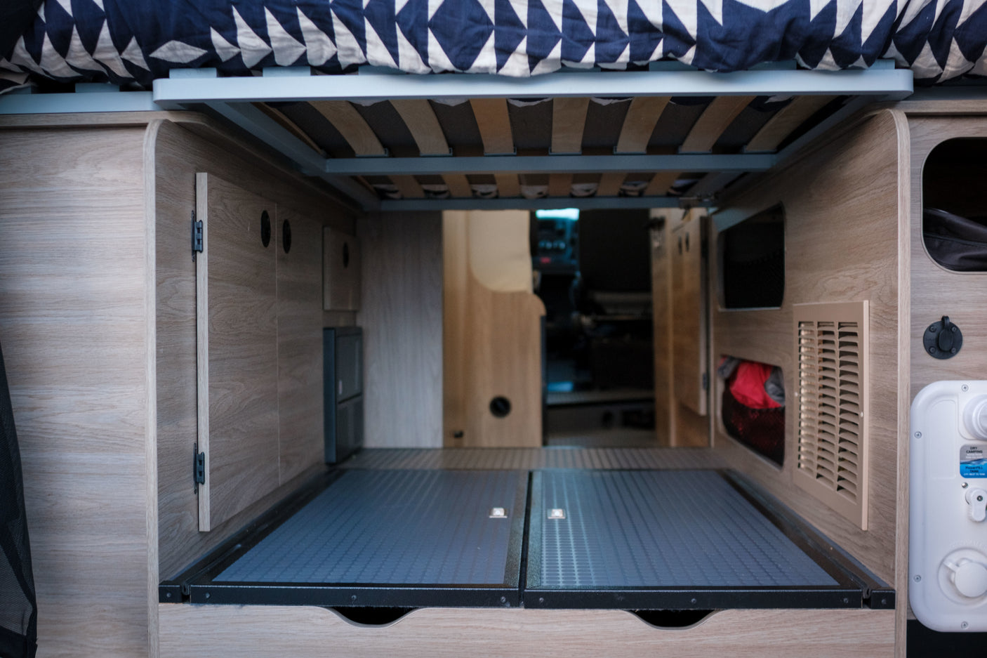 Inside an **rv rental**: organized under-bed **storage** in a **campervan**. Features wooden interior, bed frame, and utility connections.