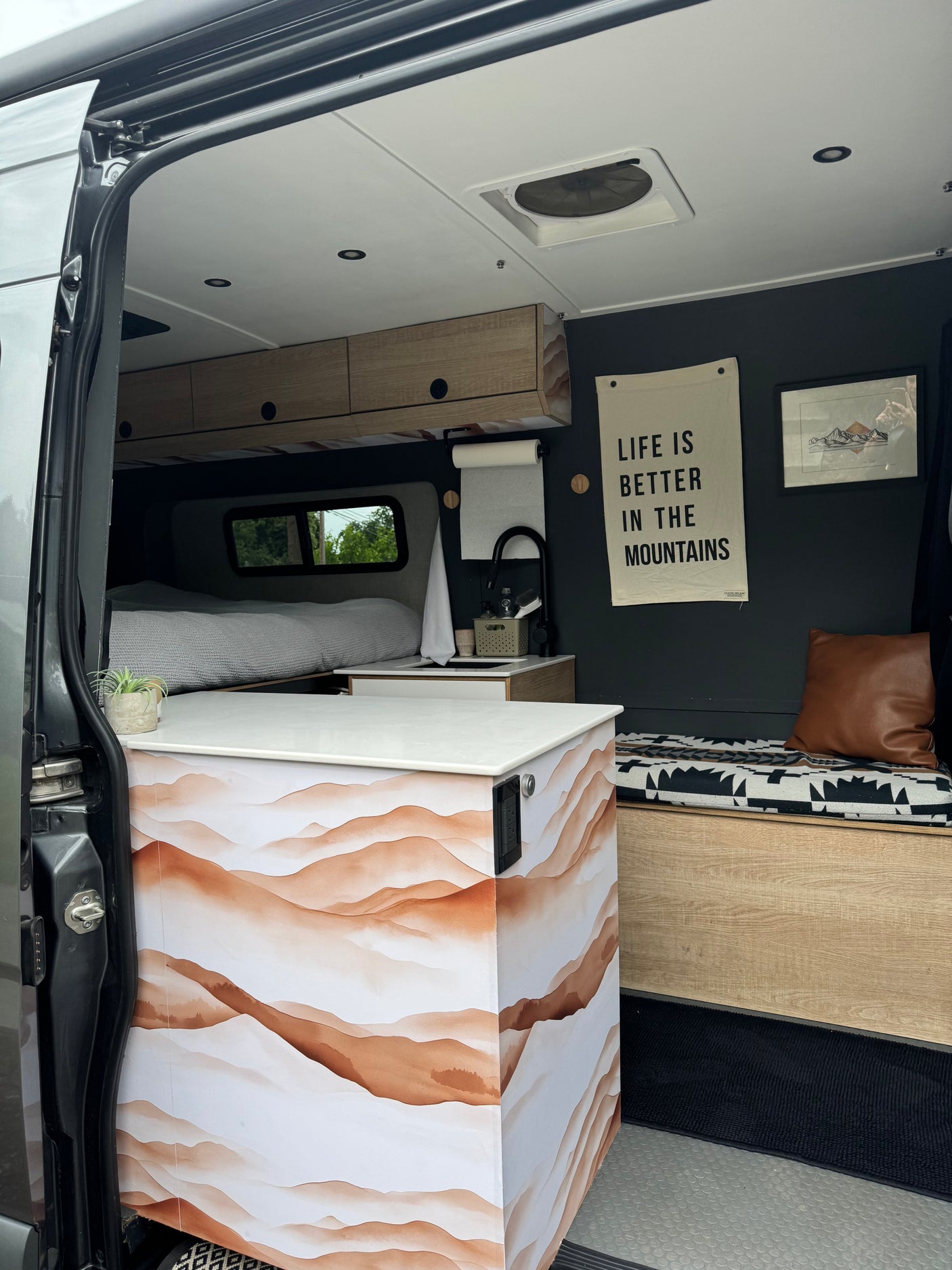 Step inside this modern camper van RV rental, showcasing a comfortable bed, kitchenette, and inviting living space.
