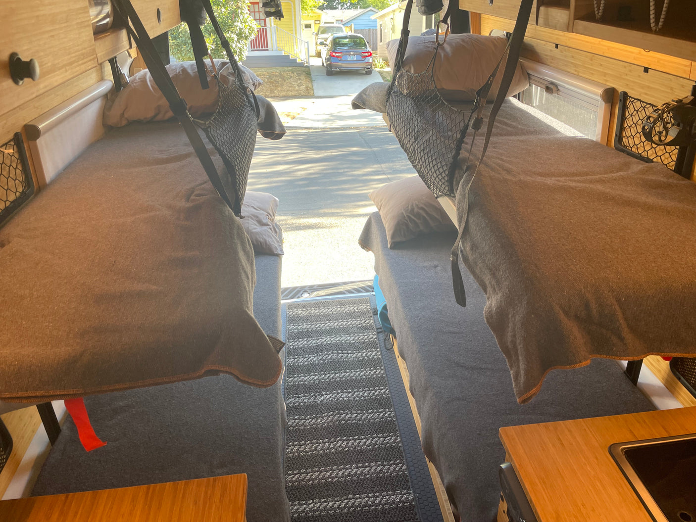 Inside a comfy RV rental: two neatly made beds, wood cabinets, and a partial kitchen area, looking out the rear.