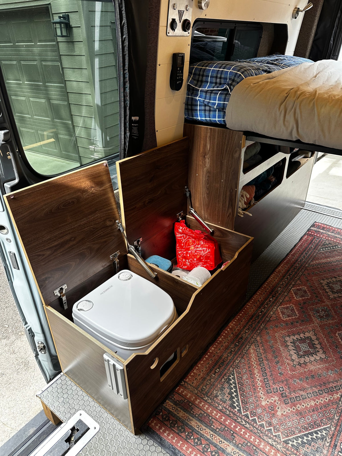 RV rental interior: Dometic portable toilet housed in a custom wooden enclosure, with a bed and integrated storage. — photo 15