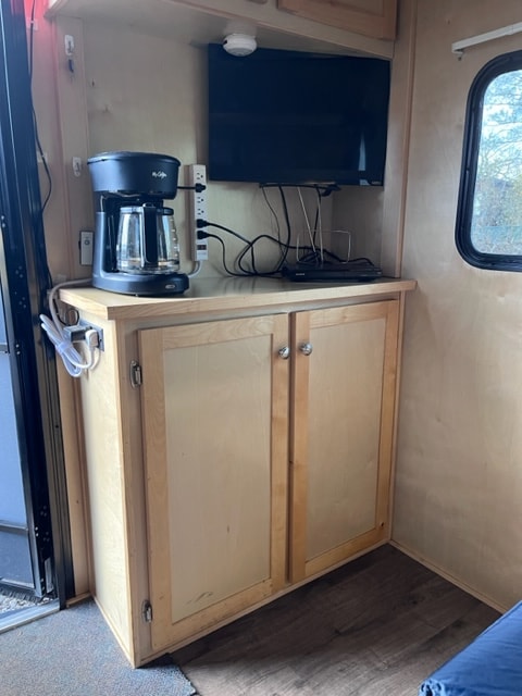 This rv rental features a built-in TV, coffee maker, power strip, and wooden storage, perfect for compact living.