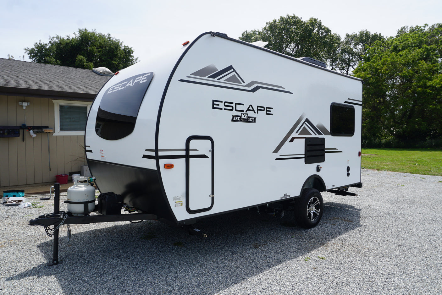 A white Escape travel trailer (RV) by KZ, parked on gravel. A versatile choice for your next rv rental.