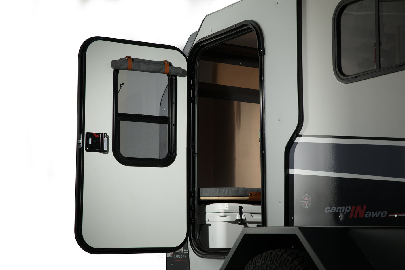 Compact RV rental: Open door shows interior bed, cooler, and roll-up shade; side has sleek stripes.