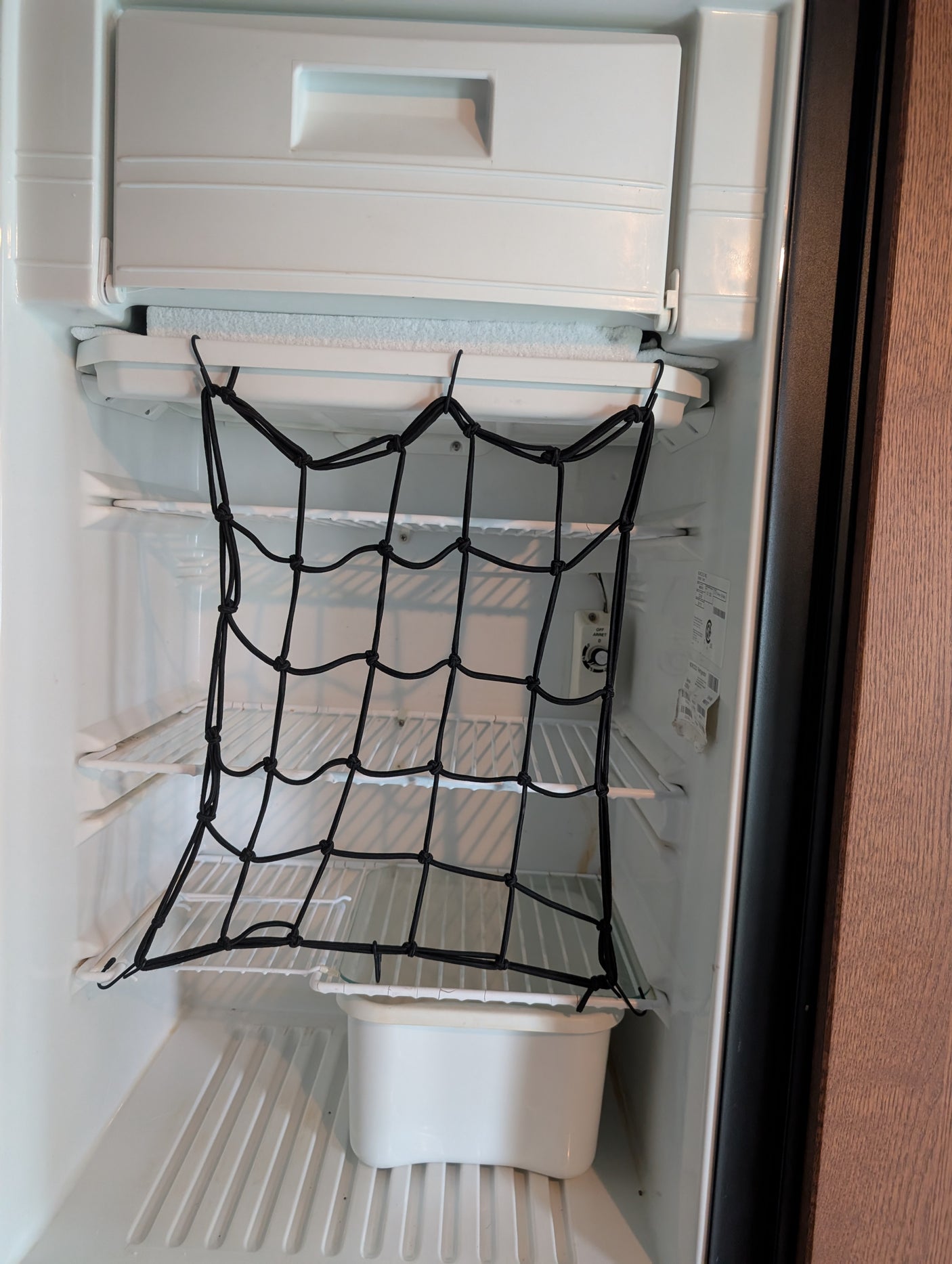 Inside an RV rental fridge: a black cargo net secures items on shelves, preventing movement & spills during travel. Frost on freezer.