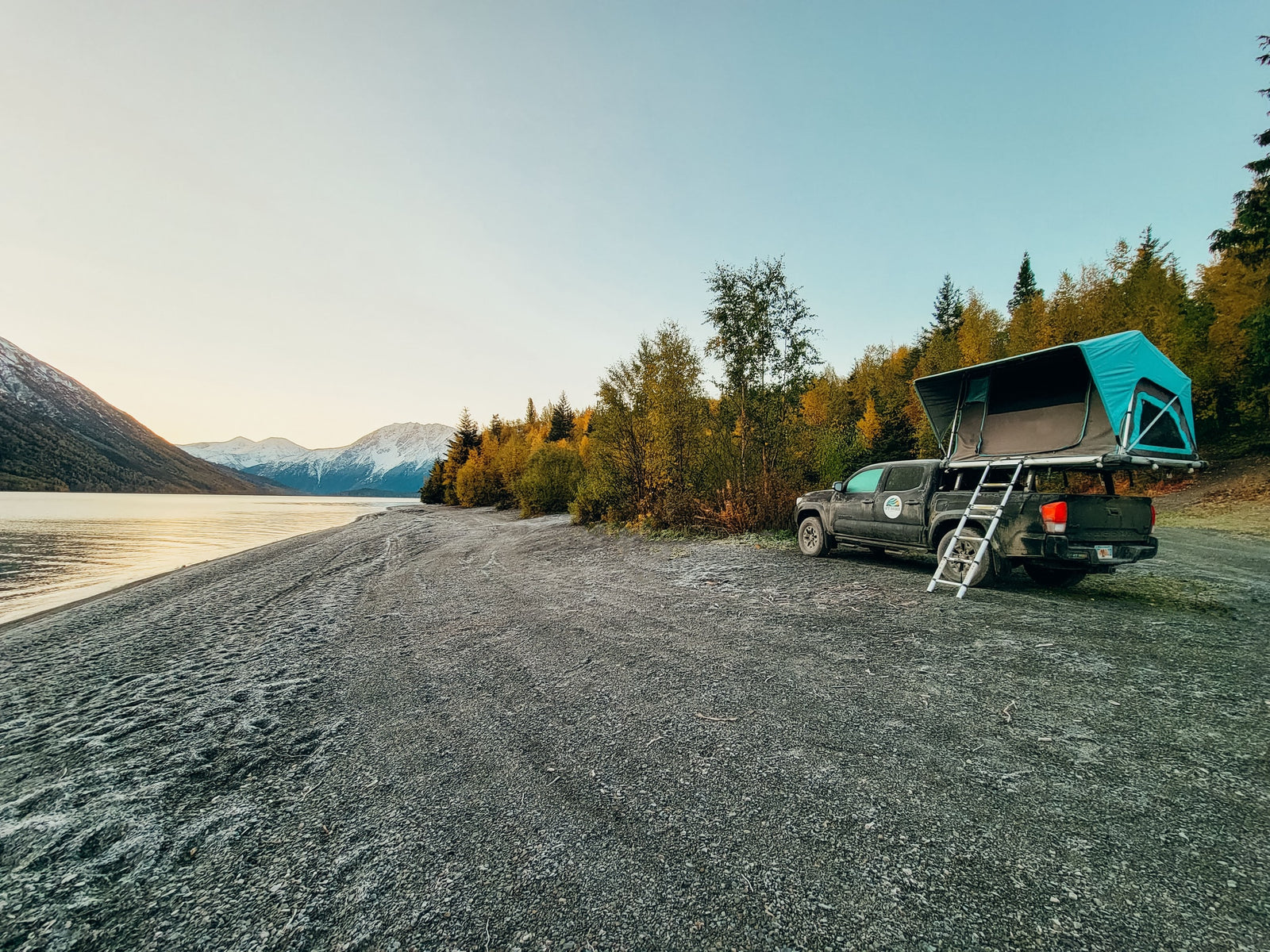Explore scenic landscapes! This RV rental setup, a truck with a rooftop tent, offers lakeside camping near snowy mountains.